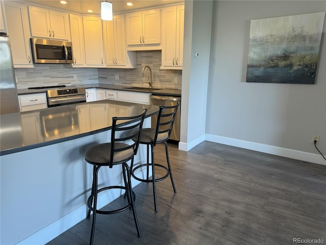 kitchen featuring stainless steel appliances, dark countertops, a sink, baseboards, and recessed lighting