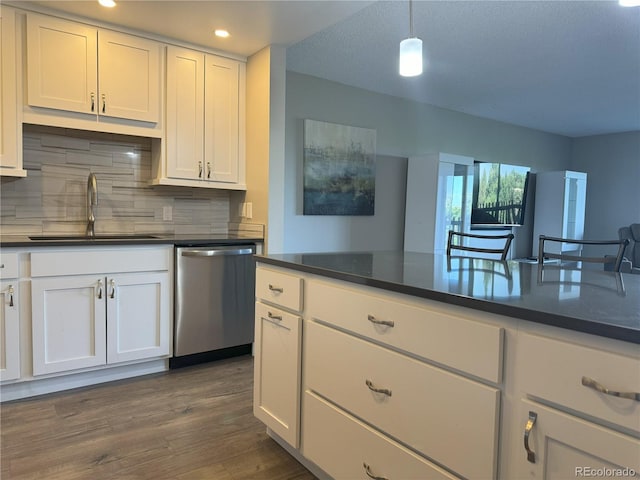 kitchen with dishwasher, a sink, dark countertops, backsplash, and white cabinetry