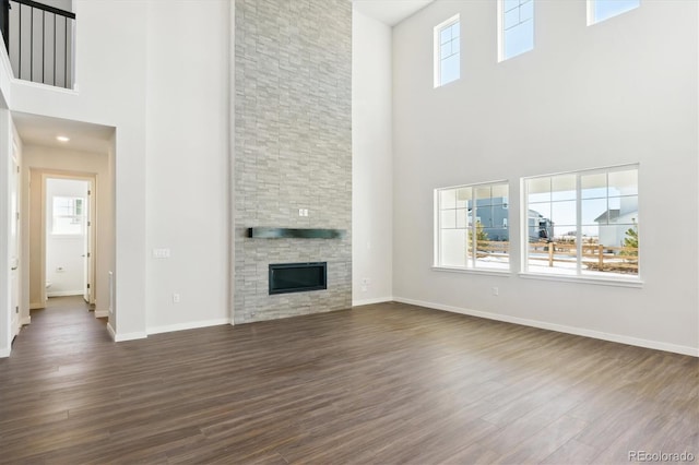 13765 Emerald Lake St, Parker, CO 80138 - unfurnished living room featuring a high ceiling, dark wood-style flooring, baseboards, and a stone fireplace