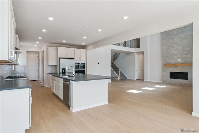 13765 Emerald Lake St, Parker, CO 80138 - kitchen featuring dark countertops, appliances with stainless steel finishes, light wood finished floors, white cabinetry, and an island with sink