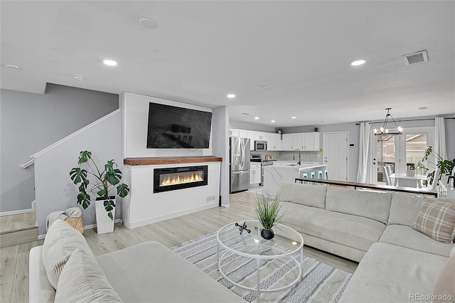 5813 Ceylon St, Denver, CO 80249 - living room featuring light wood-type flooring, a glass covered fireplace, recessed lighting, and a chandelier