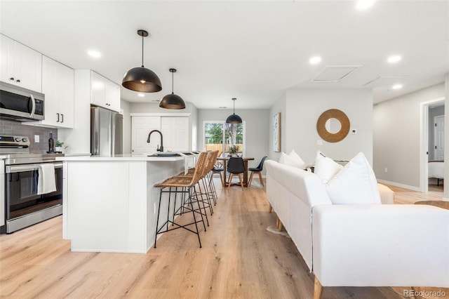 3061 S Glencoe St, Denver, CO 80222 - kitchen featuring appliances with stainless steel finishes, white cabinetry, a breakfast bar area, light wood-type flooring, and recessed lighting