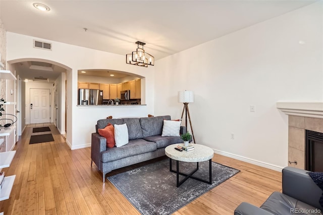 living room with a tiled fireplace, a notable chandelier, and light hardwood / wood-style flooring