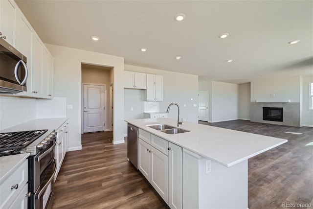 kitchen with dark hardwood / wood-style floors, sink, white cabinets, stainless steel appliances, and a center island with sink