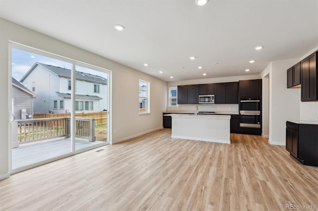 1290 Loraine Cir N, Lafayette, CO 80026 - kitchen featuring stainless steel microwave, light wood-style flooring, recessed lighting, light countertops, and an island with sink