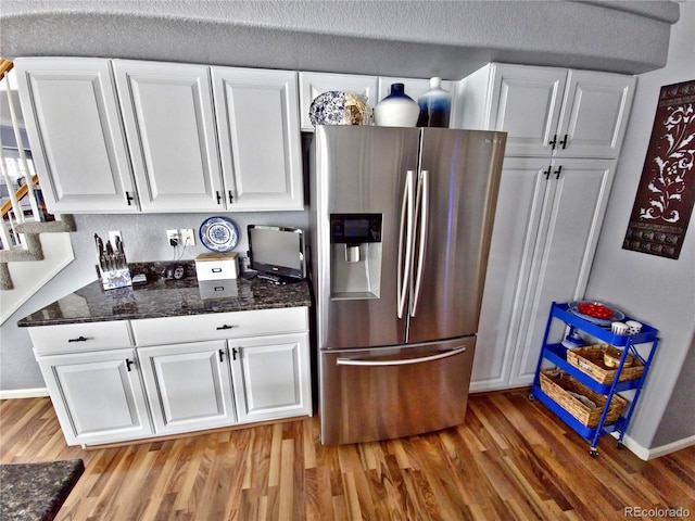 kitchen with stainless steel fridge with ice dispenser, white cabinetry, hardwood / wood-style flooring, and dark stone counters