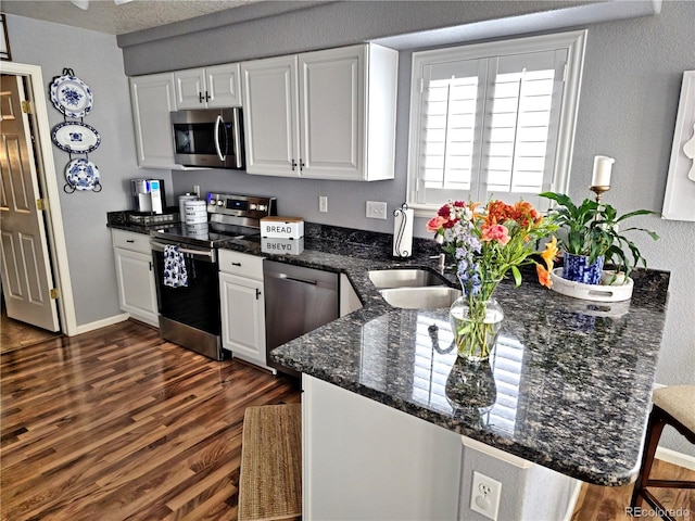 kitchen featuring white cabinetry, stainless steel appliances, dark stone counters, dark hardwood / wood-style floors, and kitchen peninsula