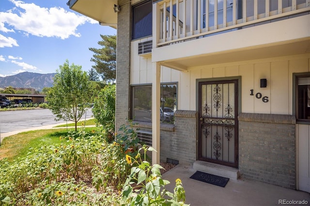 view of exterior entry featuring a mountain view, brick siding, and a balcony