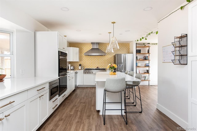 2250 N Monaco Pkwy, Denver, CO 80207 - kitchen featuring wall chimney range hood, appliances with stainless steel finishes, a kitchen breakfast bar, tasteful backsplash, and dark wood finished floors