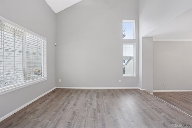 spare room with baseboards, wood finished floors, and high vaulted ceiling