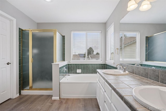 full bathroom featuring double vanity, wood finished floors, a sink, a garden tub, and a stall shower