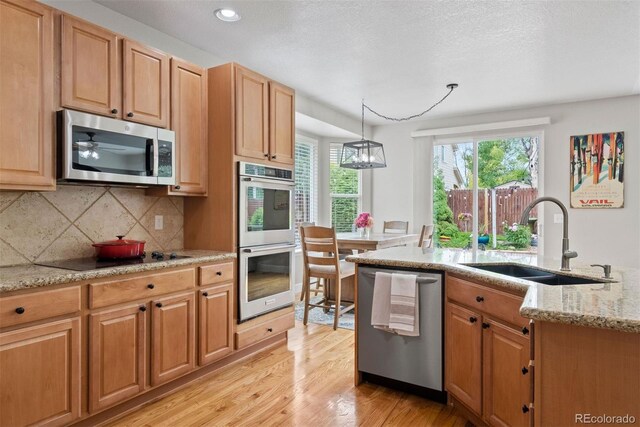 12942 Leyden St, Thornton, CO 80602 - kitchen featuring stainless steel appliances, a sink, light wood-style flooring, tasteful backsplash, and light stone countertops