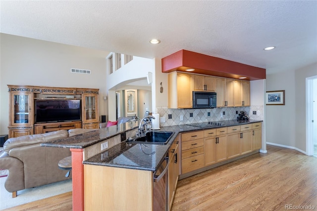 kitchen featuring sink, light hardwood / wood-style flooring, kitchen peninsula, dark stone countertops, and black appliances