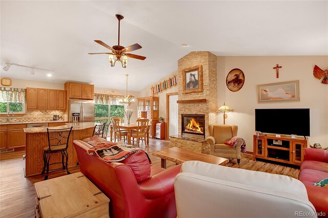 living room featuring light hardwood / wood-style flooring, ceiling fan with notable chandelier, sink, lofted ceiling, and a stone fireplace