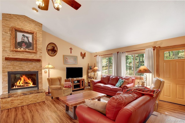 living room featuring lofted ceiling, ceiling fan, a stone fireplace, and light hardwood / wood-style floors