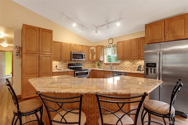 kitchen with lofted ceiling, a center island, light stone counters, and appliances with stainless steel finishes