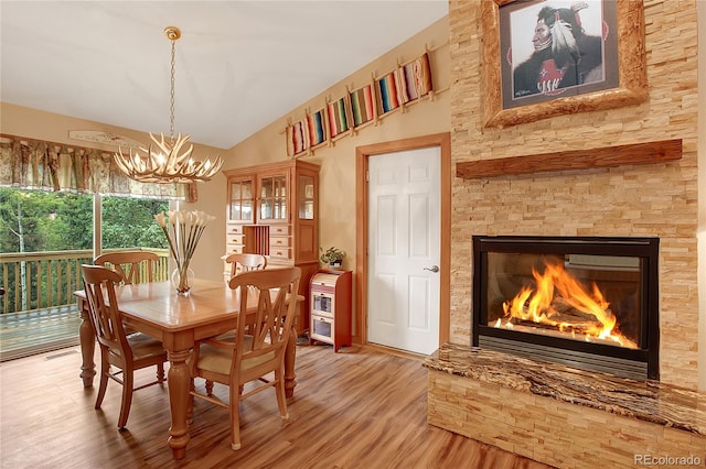 dining room with vaulted ceiling, a notable chandelier, wood-type flooring, and a fireplace