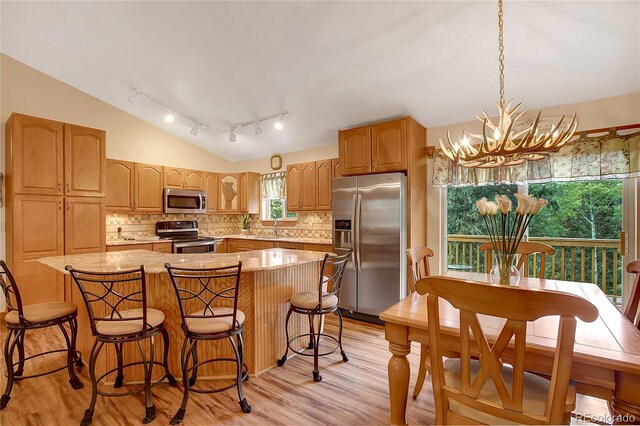 kitchen featuring a center island, vaulted ceiling, light wood-type flooring, stainless steel appliances, and a notable chandelier