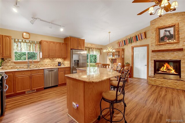 kitchen with light hardwood / wood-style flooring, stainless steel appliances, light stone counters, a center island, and a stone fireplace