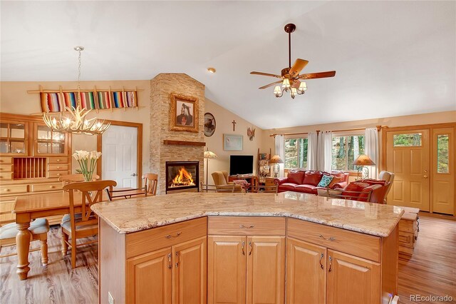 kitchen featuring light wood-type flooring, ceiling fan with notable chandelier, a center island, a stone fireplace, and lofted ceiling