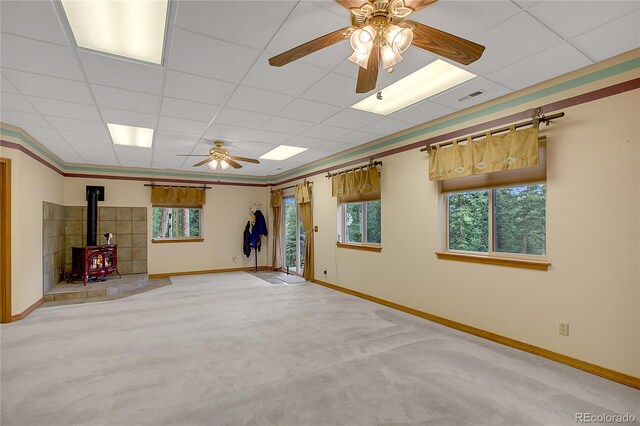 carpeted spare room with a paneled ceiling, ceiling fan, and a wood stove