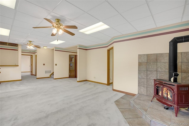 basement with light carpet, crown molding, a wood stove, and ceiling fan