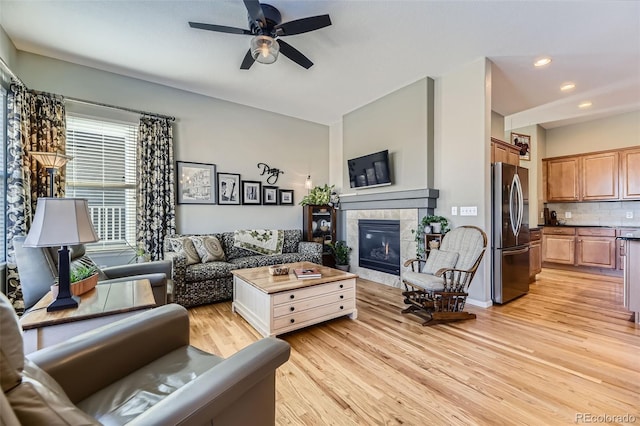 living room featuring a tile fireplace, light hardwood / wood-style flooring, and ceiling fan