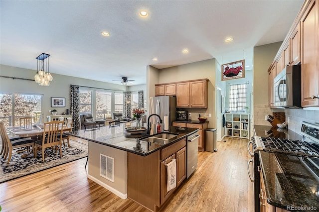 kitchen with appliances with stainless steel finishes, sink, pendant lighting, a center island with sink, and dark stone countertops