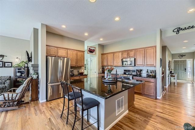 kitchen featuring a center island, dark stone counters, a kitchen breakfast bar, light hardwood / wood-style flooring, and stainless steel appliances