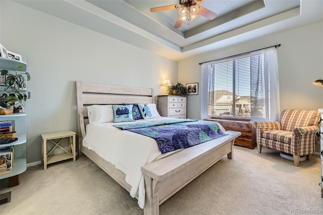 carpeted bedroom with a raised ceiling and ceiling fan