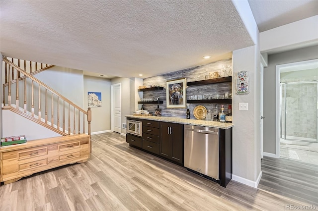 kitchen with light hardwood / wood-style flooring, light stone countertops, a textured ceiling, appliances with stainless steel finishes, and dark brown cabinets