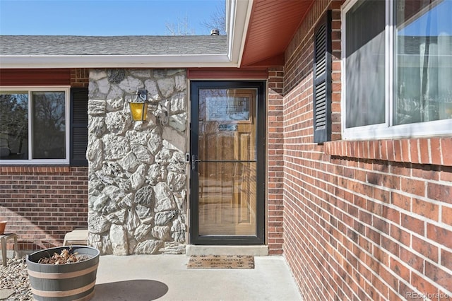 view of exterior entry featuring brick siding and roof with shingles