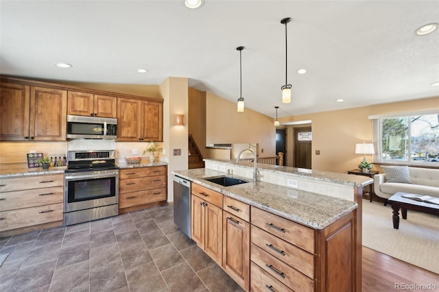 kitchen featuring light stone counters, lofted ceiling, a sink, stainless steel appliances, and open floor plan