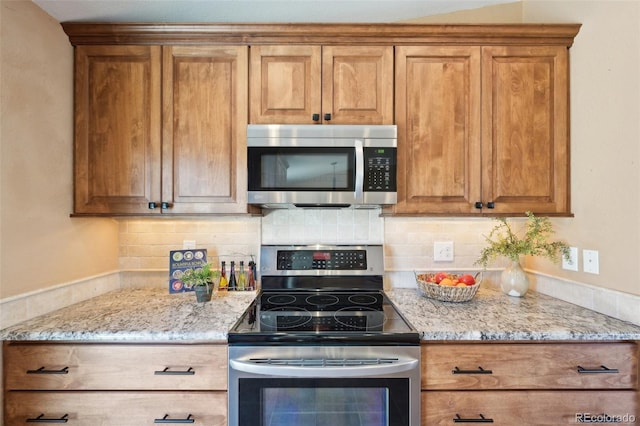 kitchen featuring light stone counters, stainless steel appliances, brown cabinets, and decorative backsplash