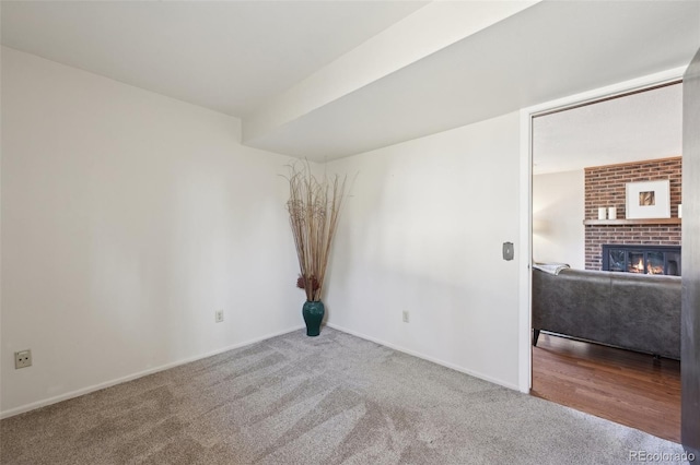 carpeted spare room featuring a fireplace and baseboards