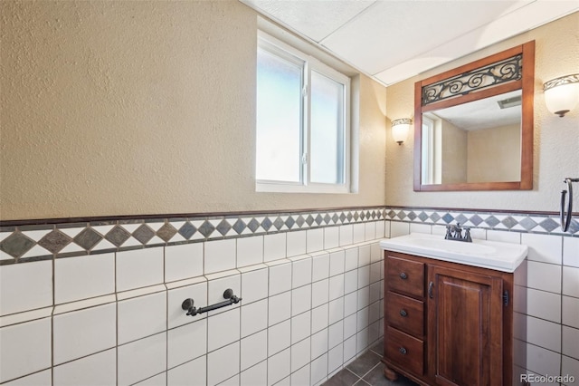 bathroom with tile walls, wainscoting, vanity, and a textured wall