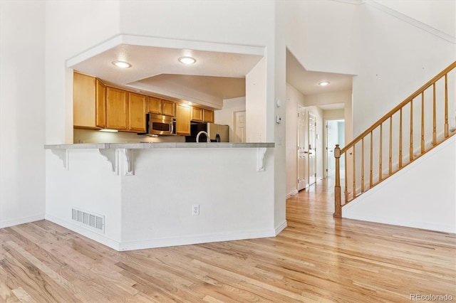 2330 S Salem Cir, Aurora, CO 80014 - kitchen with stainless steel microwave, freestanding refrigerator, a kitchen breakfast bar, light wood-style flooring, and a peninsula