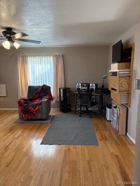 office space featuring light wood-type flooring, baseboards, a ceiling fan, and a textured ceiling