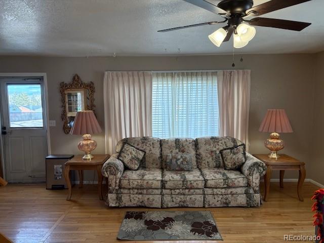 living area with light wood-style floors, a ceiling fan, baseboards, and a textured ceiling