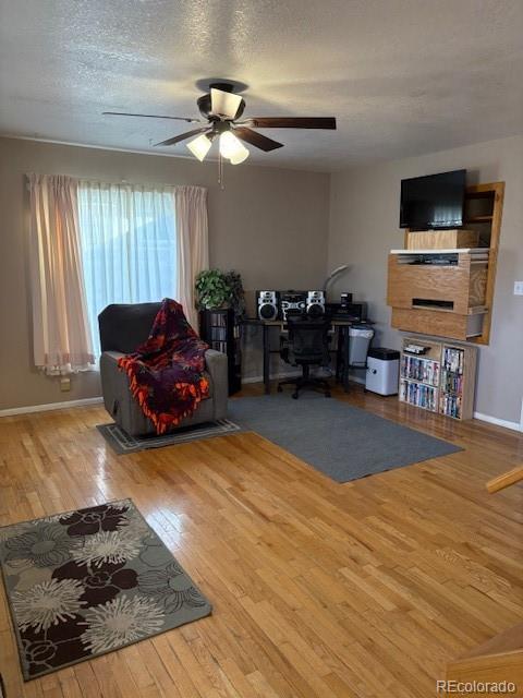 living room with a ceiling fan, a textured ceiling, baseboards, and wood finished floors