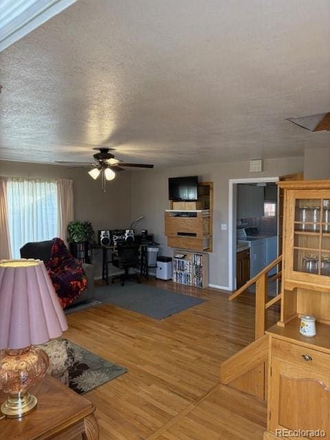 living room featuring ceiling fan, a textured ceiling, visible vents, and wood finished floors