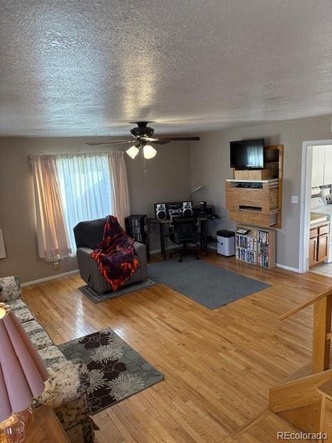 living room featuring a textured ceiling, ceiling fan, wood finished floors, and baseboards