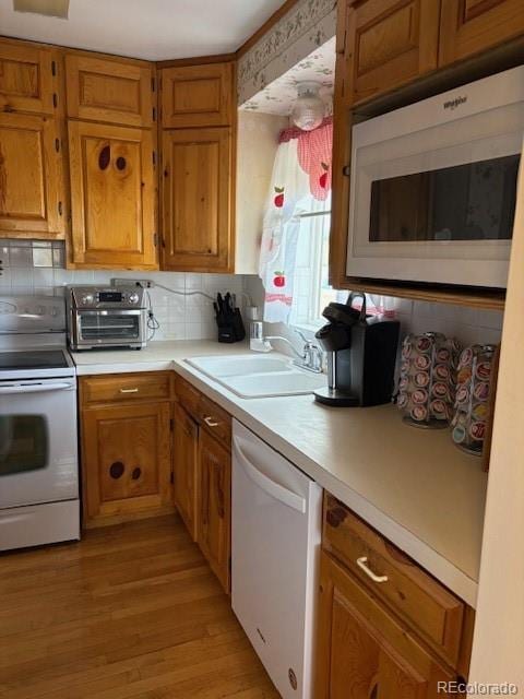 kitchen featuring brown cabinetry, white appliances, light countertops, and a sink