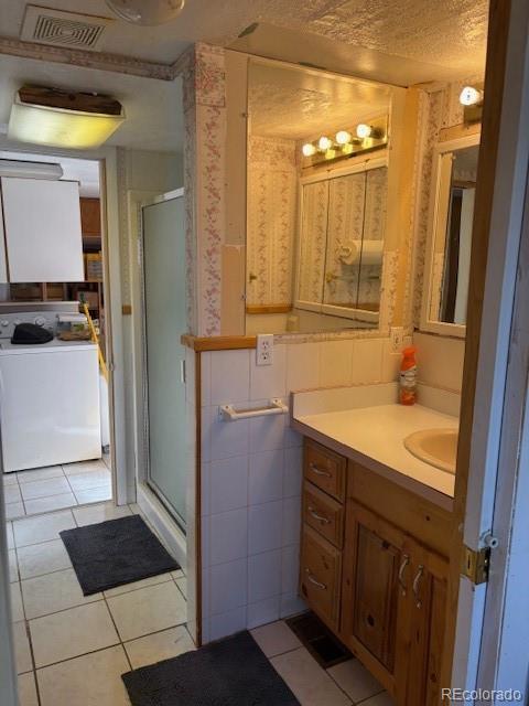 bathroom with vanity, visible vents, a shower stall, washer / clothes dryer, and wallpapered walls