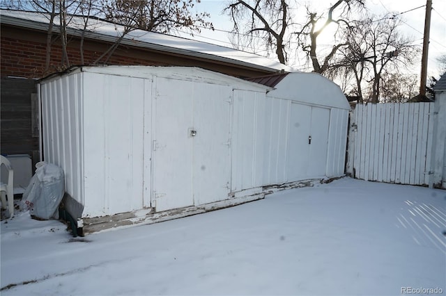 snow covered structure featuring fence and a storage unit