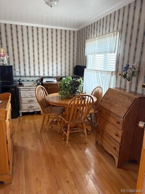 dining room featuring light wood-type flooring, wallpapered walls, and crown molding