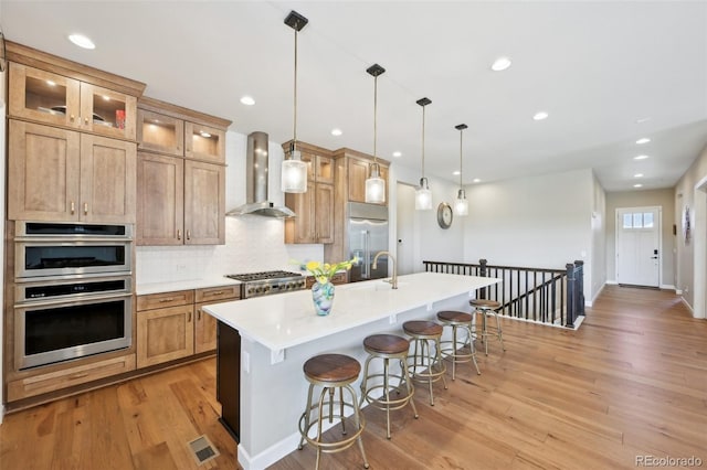 6980 S Yantley Ct, Aurora, CO 80016 - kitchen featuring appliances with stainless steel finishes, wall chimney exhaust hood, light wood-style floors, a kitchen breakfast bar, and backsplash