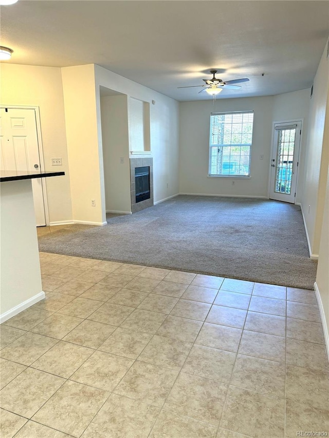 17346 Nature Walk Trl Unit 105, Parker, CO 80134 - unfurnished living room featuring light colored carpet, a ceiling fan, a tiled fireplace, baseboards, and light tile patterned flooring