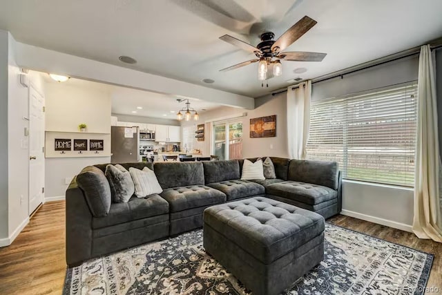 living room featuring ceiling fan with notable chandelier, a healthy amount of sunlight, and light wood-type flooring