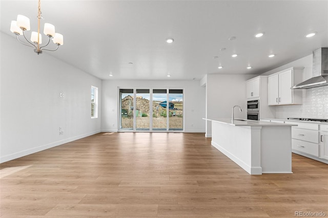 kitchen with an inviting chandelier, light hardwood / wood-style floors, gas cooktop, wall chimney range hood, and sink